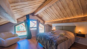 A bedroom with a sloped ceiling, a large bed, a nightstand, a chair, and a window with curtains.