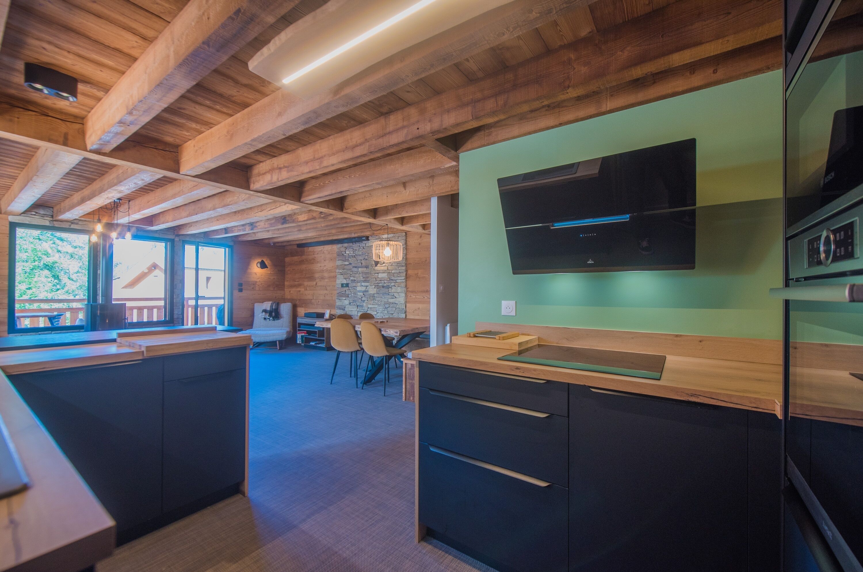 Une cuisine moderne avec des poutres en bois, un téléviseur à écran plat et un mur décoratif en pierre.