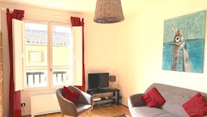A living room with a sofa, two armchairs, a TV, and a painting of a fish. - Le Jaurès - Studio Apartment, Sleeps 2 (Toulouse)