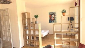A modern living room with a wooden floor, a grey sofa, a white bed, and a painting on the wall. - Le Jaurès - Studio Apartment, Sleeps 2 (Toulouse)