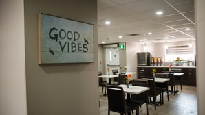 Un comedor con mesas y sillas, una cocina al fondo y un letrero que dice "GOOD VIBES".