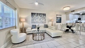 A modern living room with a sectional sofa, a glass coffee table, and a dining area with chairs. - Regal Beach Club #311 (Seven Mile Beach)