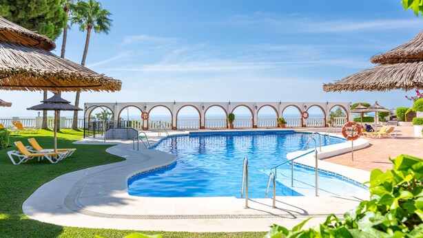 Ein Pool mit einer umlaufenden Sonnenterrasse, Liegestühlen und Sonnenschirmen.
