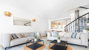 Ein modernes Wohnzimmer mit zwei Sofas, schwarzen Couchtischen und einer Treppe, die zu einer oberen Etage führt.