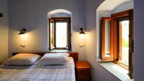 A bedroom with a bed, two bedside tables, and two windows with wooden frames.