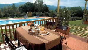 Zona de comedor junto a la piscina, con una mesa preparada para el desayuno, con vistas a una piscina y un paisaje montañoso.