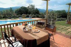 A poolside dining area with a table set for breakfast, overlooking a swimming pool and a mountainous landscape.