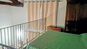 Un dormitorio con una cama verde, vigas de madera en el techo, una ventana con cortinas beige y una puerta de madera.
