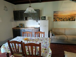 Uma área de refeições com uma mesa posta para dois, um sofá, um micro-ondas e uma geladeira ao fundo.