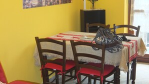 Een eetgedeelte met een tafel voor vier personen, houten stoelen, een rode kussen en een schilderij van een berglandschap aan de muur.
