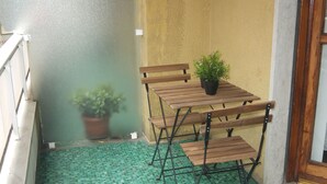 Een klein terras met een houten tafel en stoelen, een potplant en een vloer van groene tegels.