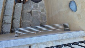 Una escalera de piedra que conduce a una puerta de madera con un ventanal, barandilla metálica y un toldo azul.