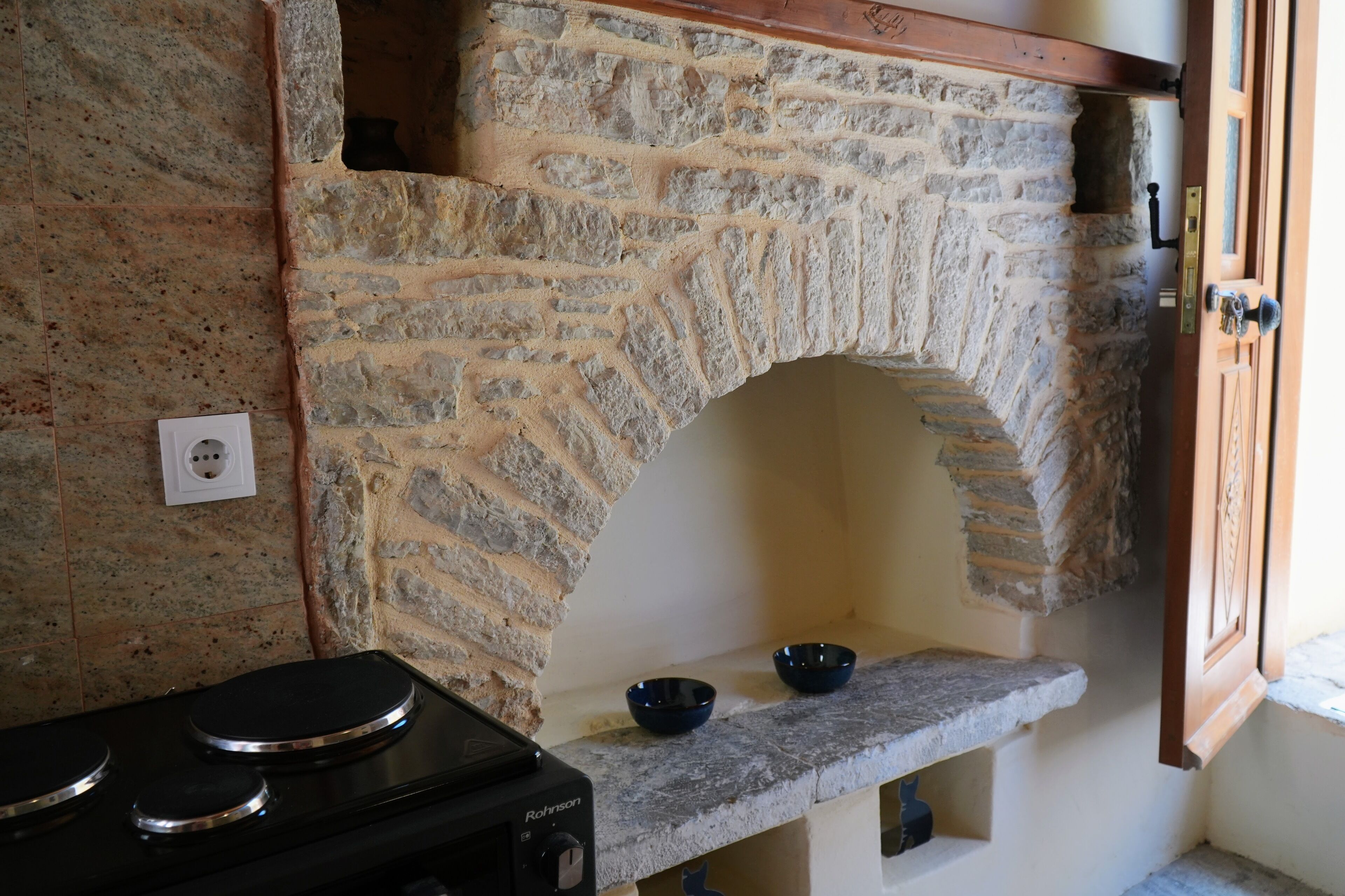 A kitchen with a stone arch fireplace, a stove, and two bowls on a shelf.