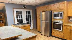 A kitchen with wooden cabinets, a stainless steel refrigerator, a microwave, and an oven. - Quiet farmhouse with amazing views - close to skiing in Ellicotville! (Little Valley)