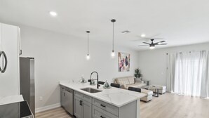 Una cocina moderna con una isla central, un área de comedor con un sofá y una mesa de centro, y un ventilador de techo.