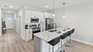 Una cocina moderna con armarios blancos, electrodomésticos de acero inoxidable y una isla de mármol con taburetes de bar.