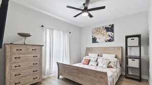 Un dormitorio con cama de madera, cómoda, ventilador de techo y altavoz en la pared.