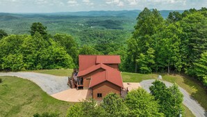 Une cabane en rondins avec un toit rouge, entourée d’une végétation luxuriante et bordée d’une allée de gravier.