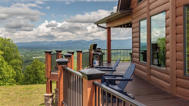 Une terrasse en bois avec coin salon extérieur et barbecue, offrant une vue sur un paysage montagneux.