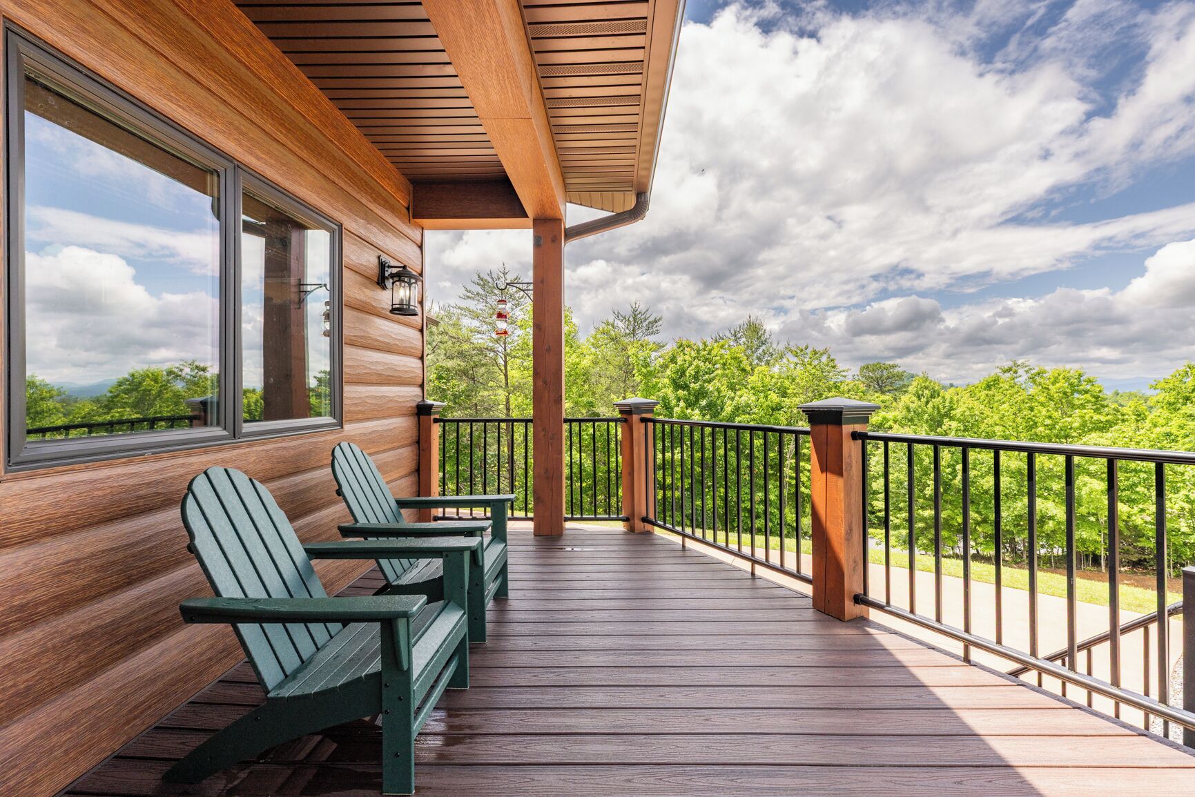 A wooden deck with Adirondack chairs, a railing, and a view of trees and sky.