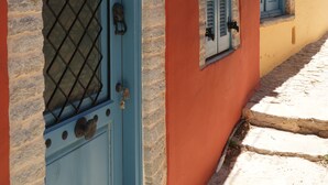 Un edificio con puerta y contraventanas azules, escalones de piedra y pared roja.