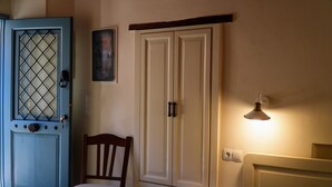 Una habitación con puerta azul, un armario blanco, una silla de madera, una lámpara de noche y una toalla blanca sobre la cama.