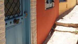 Un edificio con puerta y contraventanas azules, pared de piedra y un camino adoquinado.