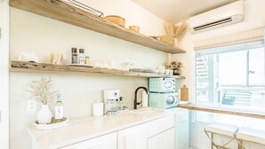 Una cucina con mobili bianchi, uno scaffale in legno, una macchina da caffè e una finestra con vista.