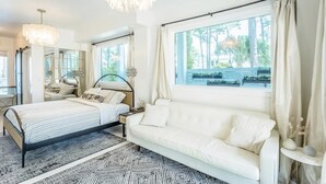 Una camera da letto con un letto, un divano, un lampadario e un'ampia finestra con tende.