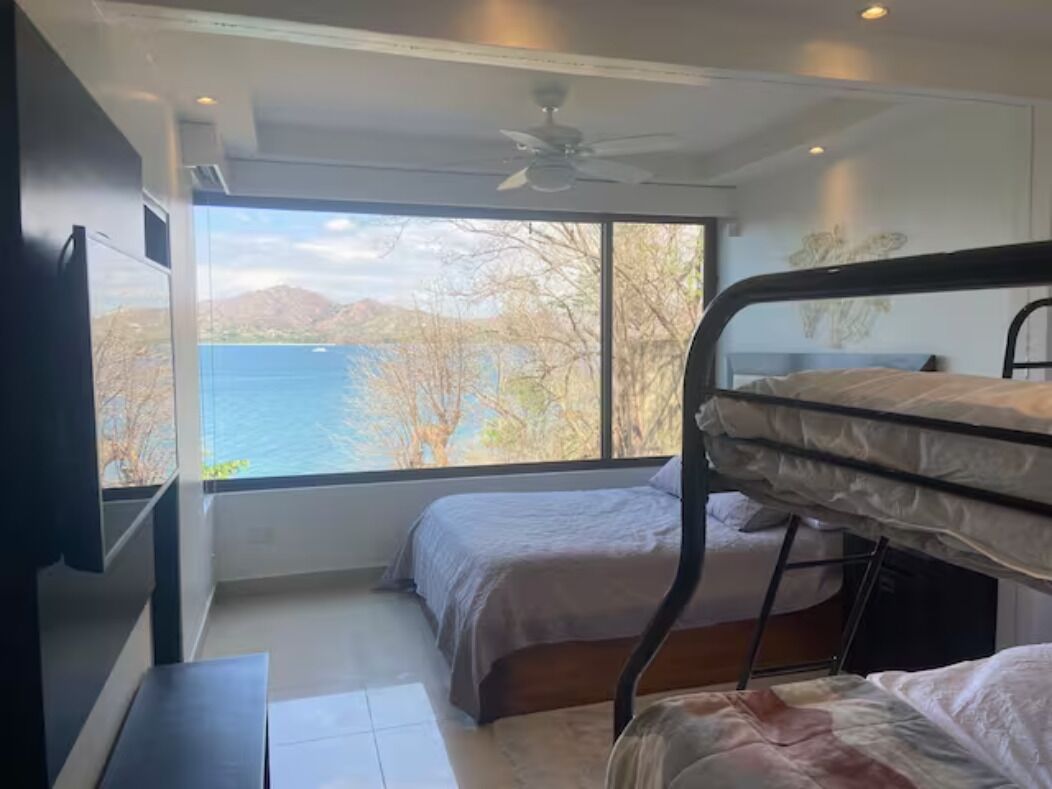 Une chambre avec des lits superposés, une télévision et une grande fenêtre donnant sur un lac et des montagnes.