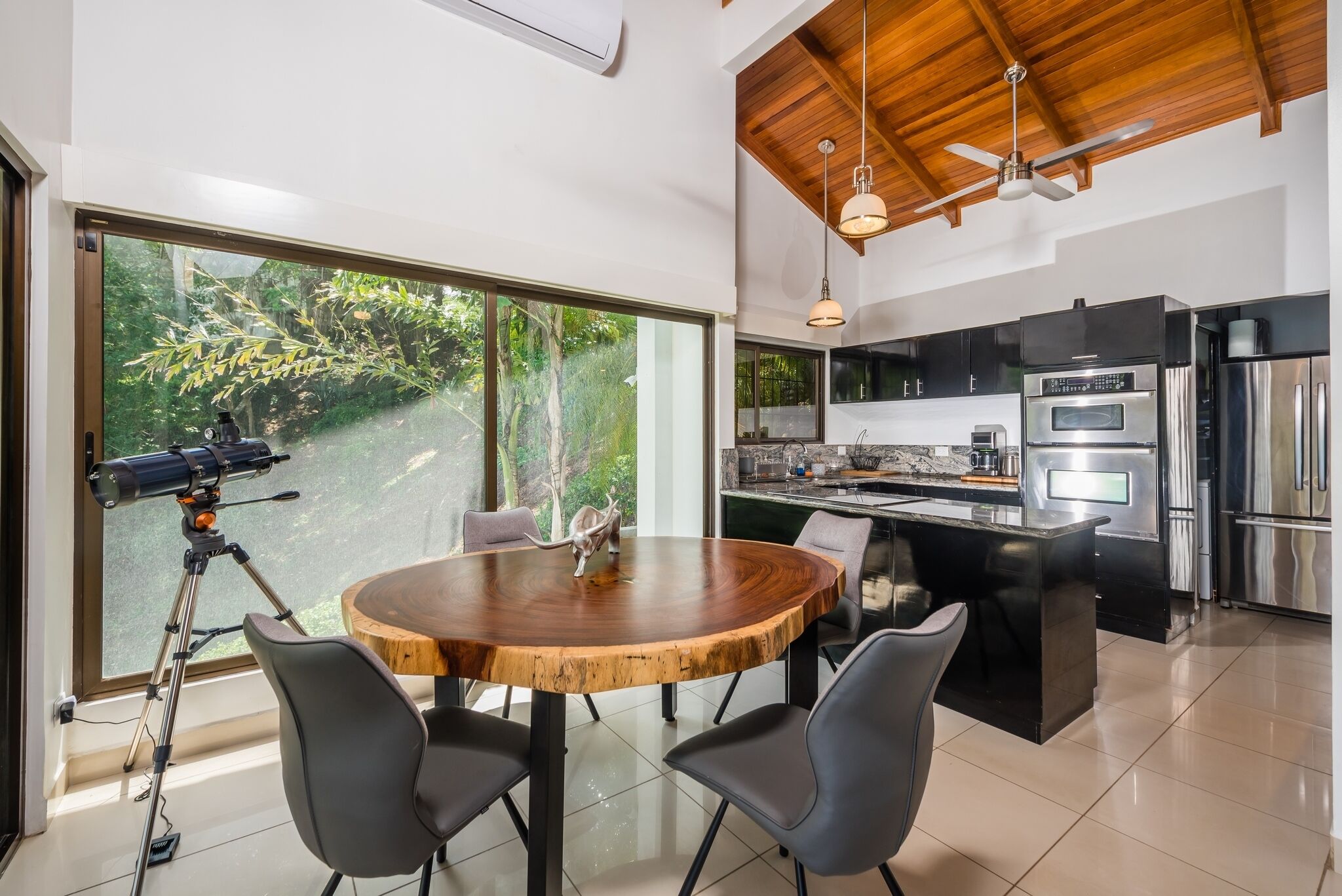 Una cocina moderna con una isla central, ventanas amplias y un telescopio sobre trípode.