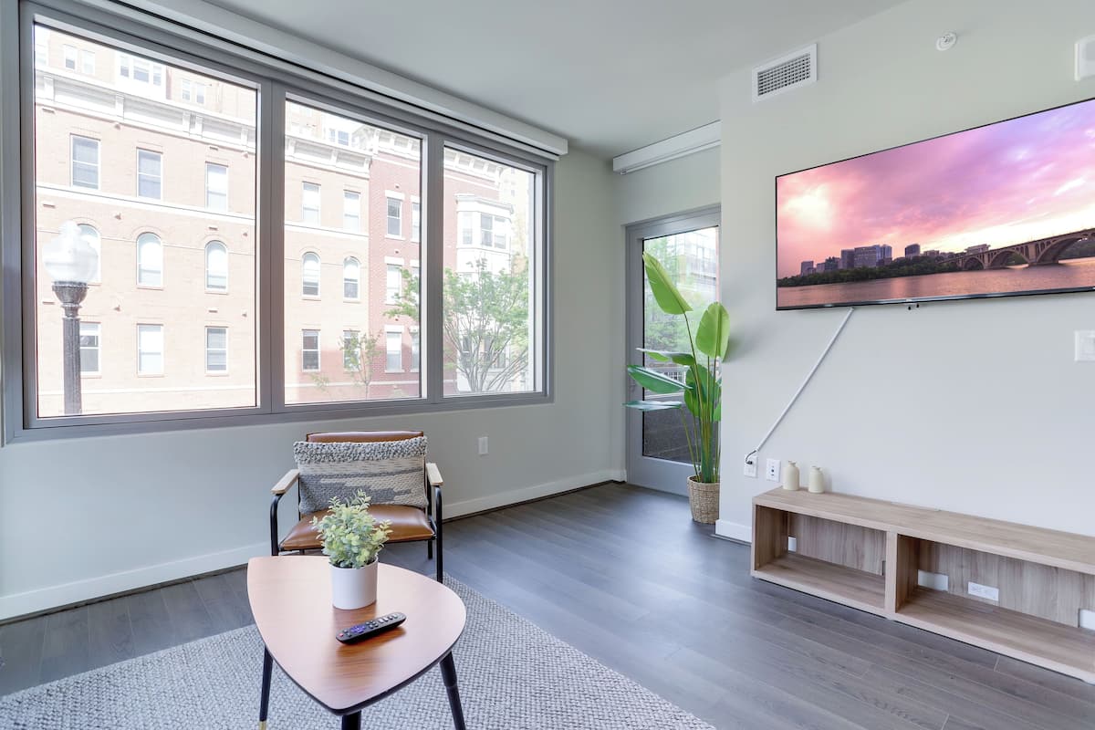 A modern living room with a large window, a flat-screen TV, a sofa, a coffee table, and a plant.