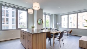 A modern kitchen with a central island, large windows, and a dining area with chairs and a table. - Cozy Apartments Near the Metro (Arlington)