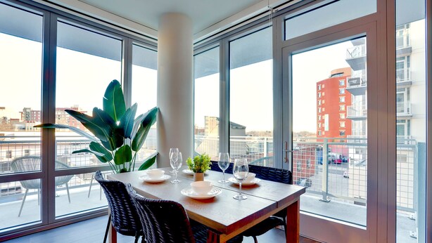 A dining area with a table set for four, large windows, and a view of the cityscape. - Cozy Apartments Near the Metro (Arlington)
