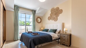 Un dormitorio con cama, mesitas de noche, una ventana con cortinas y un adorno en la pared.