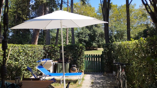 A garden with a white umbrella, a blue lounge chair, and a gate. - Duna house in the green, relaxing terratet halfway between the sea and the countryside (Donoratico)