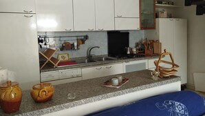 A kitchen with white cabinets, a granite countertop, and a sink. There are two ceramic pots on the counter, a coffee maker, and a wooden utensil holder. - Duna house in the green, relaxing terratet halfway between the sea and the countryside (Donoratico)