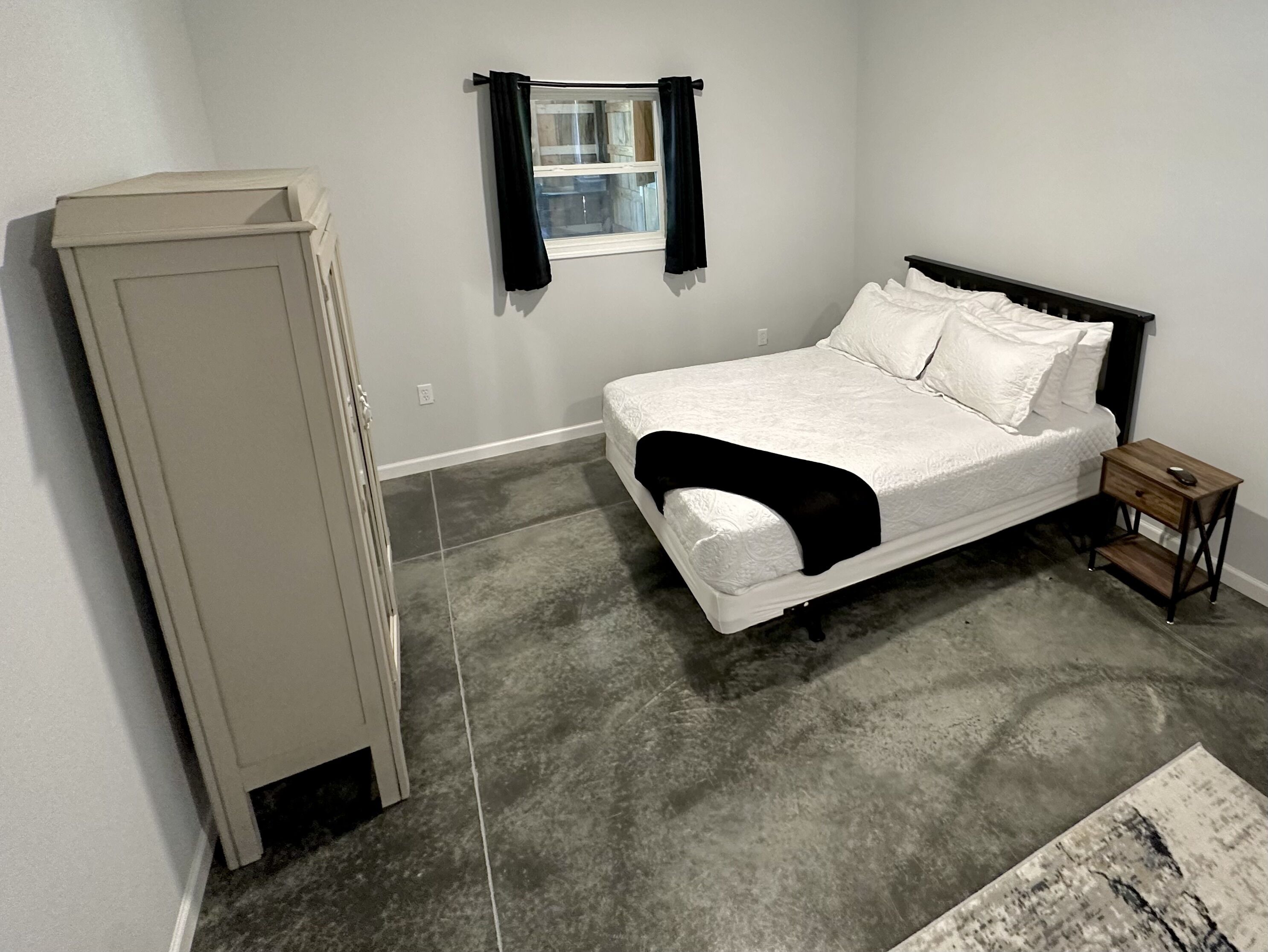 A bedroom with a bed, a nightstand, a wardrobe, and a window with curtains.