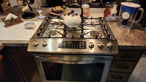 A kitchen with a stainless steel stove, a digital clock, and various kitchen items on the countertop. - At Paradise in the Valley (Palmer)