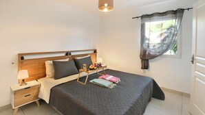Une chambre bien rangée, avec un lit, une table de chevet, une lampe et une fenêtre avec des rideaux.