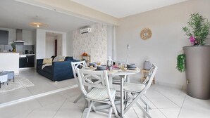 Un salon moderne comprenant un coin repas, une cuisine et un grand pot de fleurs gris.
