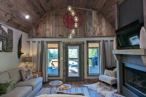 Un interno rustico con soffitto in legno, un orologio grande, un camino e un’area salotto accogliente con divano e poltrone.