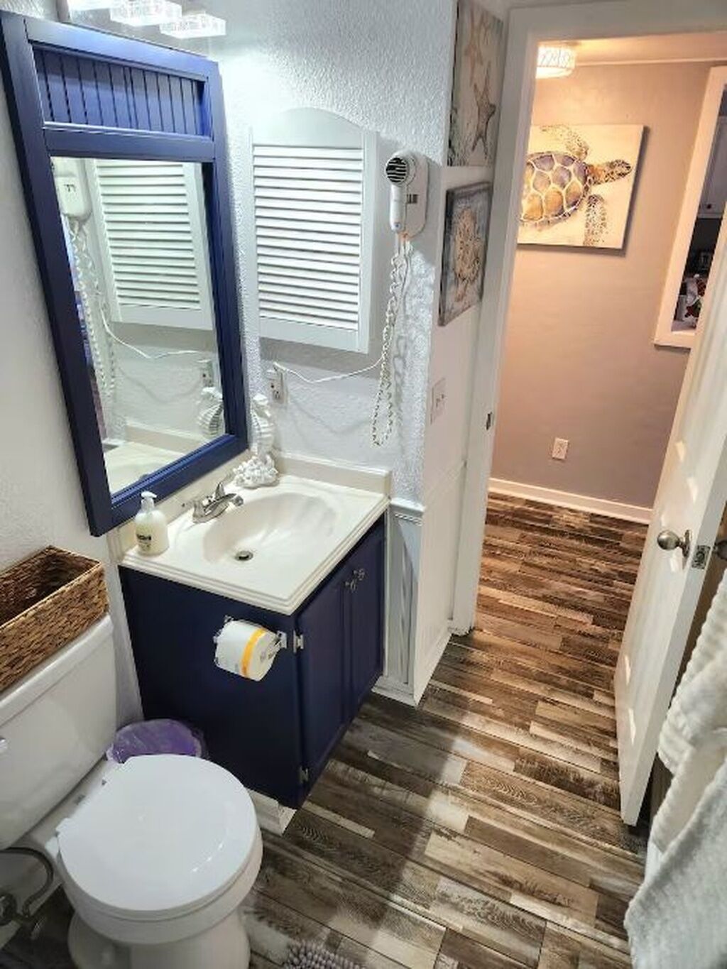 Un baño con inodoro blanco, tocador azul, lavabo blanco y espejo.