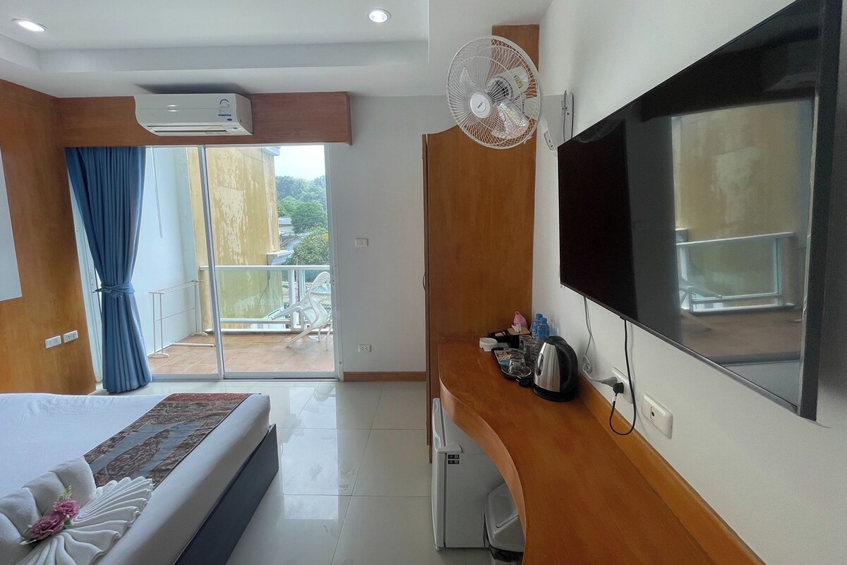 A hotel room with a bed, a TV, a small kitchenette, and a balcony with a view.