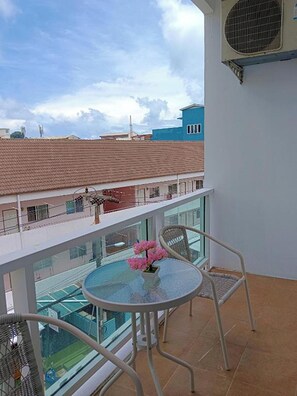 A balcony with a glass table and chairs, overlooking a swimming pool and buildings. - T & C Hotel Patong Beach By Zuzu (Patong)