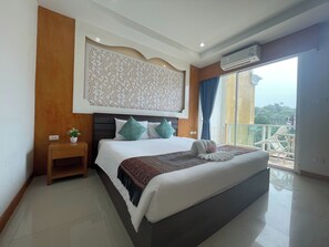 A modern hotel room with a large bed, a decorative wall panel, a small bedside table with a plant, and a balcony with a view. - T & C Hotel Patong Beach By Zuzu (Patong)