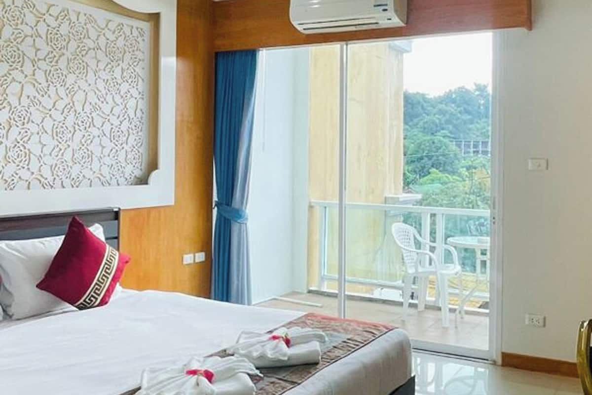 A hotel room with a large bed, a balcony with white chairs, and an air conditioning unit.
