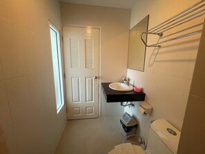 A small, clean bathroom with a white door, a black sink, a mirror, and a toilet. - T & C Hotel Patong Beach By Zuzu (Patong)