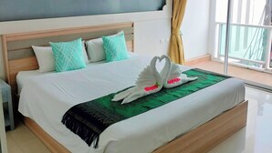 Habitación de hotel con una cama grande, cabecera de madera, manta verde y un cisne decorativo hecho con almohadas.