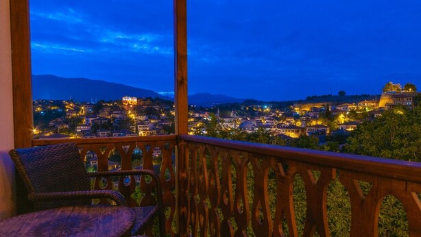 A balcony with a view of a town at dusk, featuring a wooden railing and wicker chairs. - Manzara Konak Otel (Safranbolu)